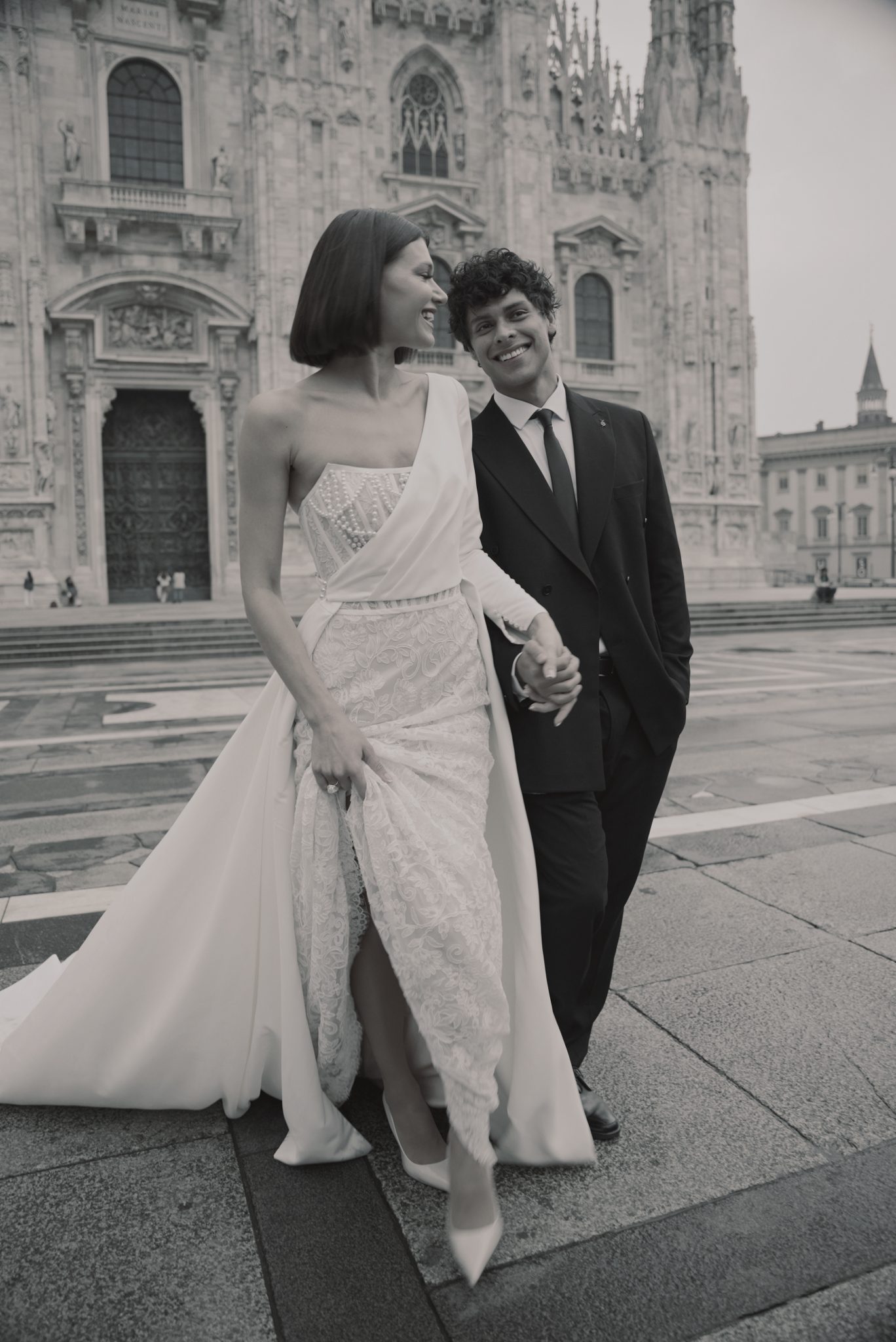 Bride and groom walking hand in hand in front of the Duomo di Milano, captured in an editorial-style wedding shoot.